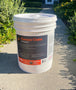 a 5 gallon pail of greasegone degreaser which is sitting on a concrete walkway between some bushes